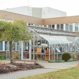A greenhouse attached to a building surrounded by a landscaped area.