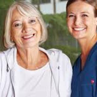 An elderly woman smiling alongside a nurse in an outdoor setting.