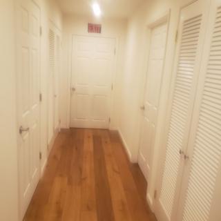 A well-lit hallway with multiple doors and a wooden floor.