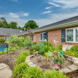 A well-maintained garden in front of a brick house, featuring a variety of plants and a decorative bench.