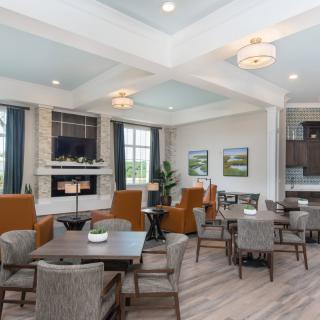 A modern living room with comfortable seating, tables, and a fireplace, illuminated by natural light from large windows.