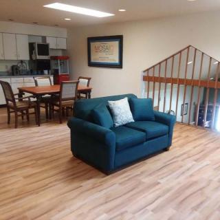 A cozy living and dining area with a teal sofa, wooden floors, and an open kitchen space.