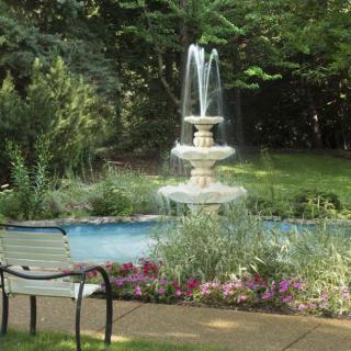 A peaceful garden scene with a flowing fountain and a bench surrounded by lush greenery and colorful flowers.