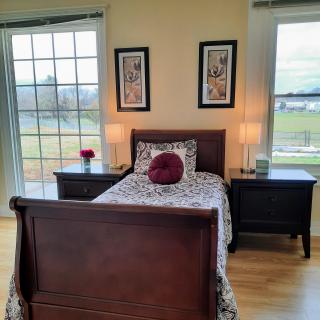A cozy bedroom with a single bed, two nightstands, and large windows providing ample daylight.