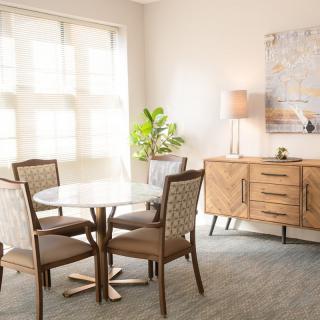 A bright dining room featuring a round table with four chairs, a sideboard with a lamp and plant, and wall art in a modern interior design.
