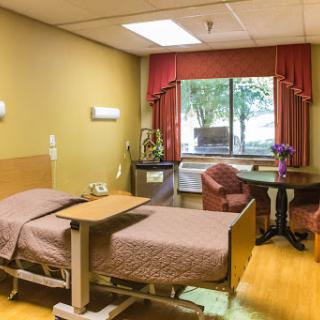 A cozy hospital patient room featuring a bed, seating area, and window with natural light.