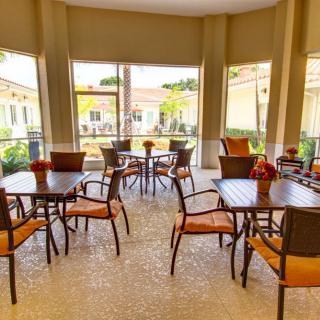 A bright and inviting indoor cafe with several tables and chairs, surrounded by large windows.