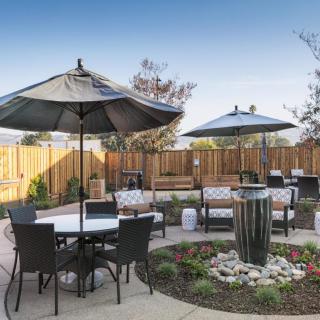 A modern outdoor patio area with tables, chairs, and umbrellas surrounded by landscaped garden features.