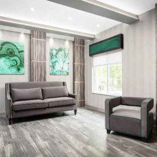 A modern living room with a grey sofa and armchair, complemented by abstract artwork and ample natural light.