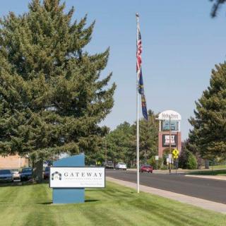 An office building with a sign and flagpole surrounded by trees on a sunny day.