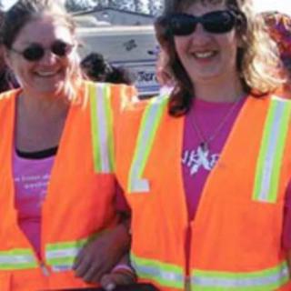 Two women wearing safety vests and sunglasses outdoors.