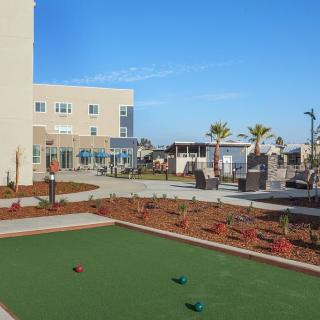 A sunny day at a modern building with an outdoor bocce court and landscaped surroundings.