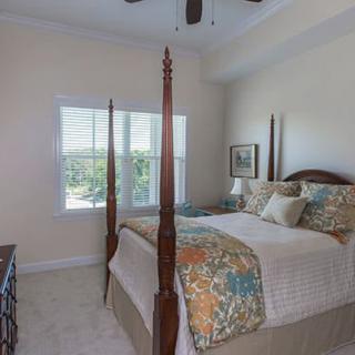 A cozy bedroom featuring a four-poster bed with patterned bedding, soft lighting, and a window letting in natural light.