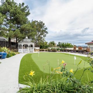 A beautifully landscaped garden featuring a gazebo, vibrant green grass, and blooming flowers under a partly cloudy sky.