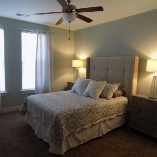 A cozy bedroom with a neatly made bed, two lamps on nightstands, and large windows with curtains.