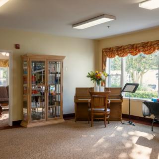 A cozy living space with a piano and bookshelf, illuminated by sunlight streaming through the window.