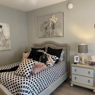 A stylishly decorated bedroom with a patterned bedspread, multiple pillows, and elegant artwork on the walls.