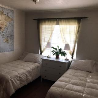A cozy bedroom with two twin beds, featuring a world map on the wall and a sunlit window.