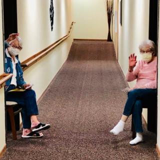 Two people wearing masks engage in a socially-distanced conversation in a hallway.
