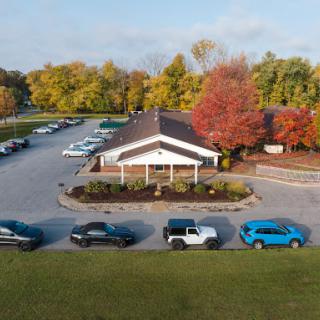 Aerial view of a building surrounded by autumn trees and a busy parking lot.