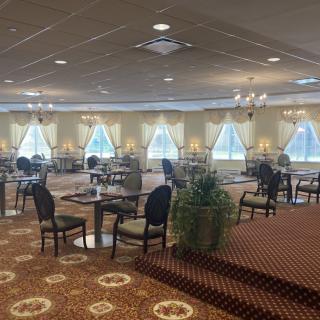 A spacious dining area with neatly arranged tables and chairs, adorned with chandeliers and large windows with curtains.