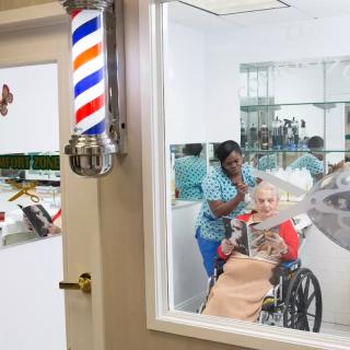 A senior man in a wheelchair receives a haircut at a barbershop, assisted by a friendly barber.