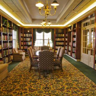 A cozy library room with bookshelves, a large table, and comfortable chairs.