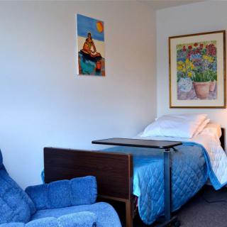A room with a hospital bed and a blue armchair, decorated with artwork on the walls.