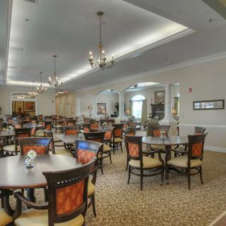 A spacious dining room with elegantly arranged tables and chairs, featuring chandeliers and a plush carpet.