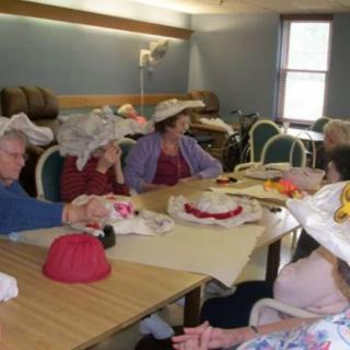 A group of elderly individuals gathered around a table wearing decorative hats.