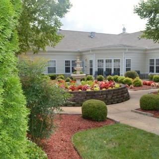 A beautifully landscaped garden with a central fountain and pathway leading to a building.