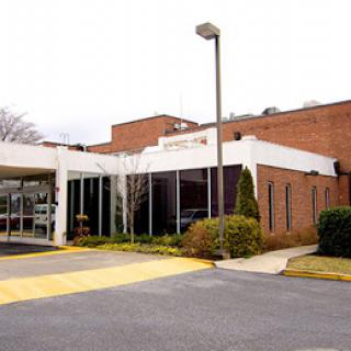 A modern commercial building with a parking area and landscaped surroundings.