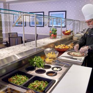 A chef preparing a dish at a buffet counter with various ingredients on display.