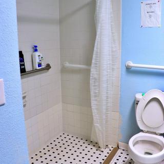 An accessible bathroom with a shower and toilet, featuring grab bars and a tiled floor.