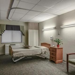 A neatly arranged hospital room with a single bed, a chair, and a bedside drawer.