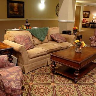A cozy living room with a sofa, armchair, and wooden coffee table arranged on a patterned carpet.