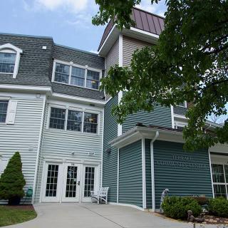 A residential building with a light blue exterior and multiple windows, surrounded by trees.