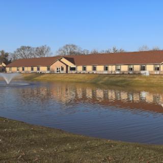 A peaceful residential building reflecting in the calm waters of a pond on a clear day.