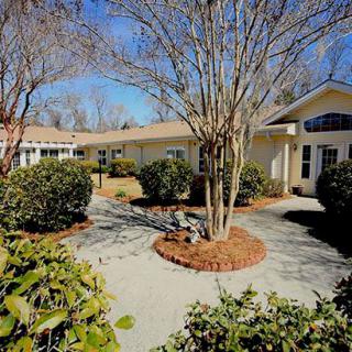 A sunny view of a building exterior with a garden and pathway lined with shrubs and trees.