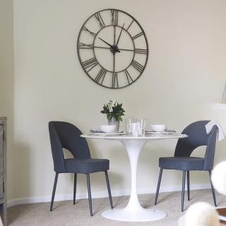 A modern dining area with a round table and two chairs, adorned with a large wall clock.