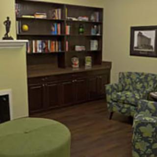 A cozy living room featuring a bookshelf, patterned chairs, and a green ottoman.
