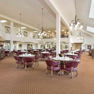 A spacious dining hall with neatly arranged tables and chairs, illuminated by elegant chandeliers.