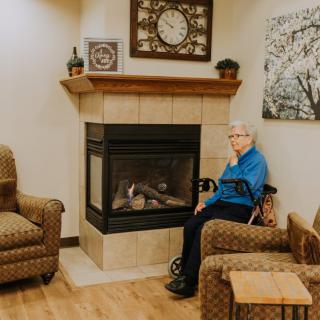 An elderly person sitting by a fireplace in a cozy living room.