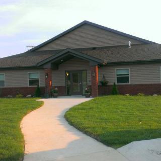 A single-story residential house with a well-maintained lawn and a curving concrete pathway leading to the entrance.
