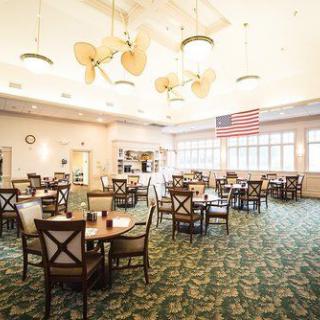 A spacious dining area with tables and chairs, featuring ceiling lights and a large flag on the wall.