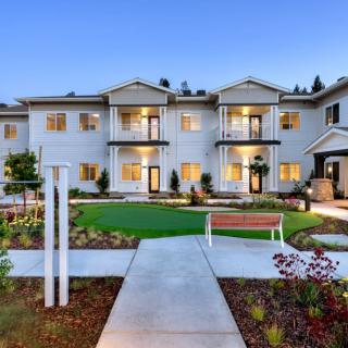 A well-maintained apartment building with landscaped gardens and a paved walkway during the evening.