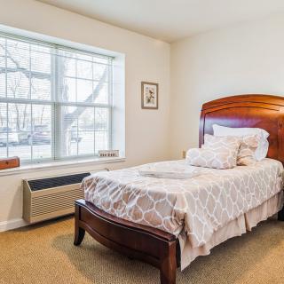 A cozy bedroom featuring a single bed with decorative pillows and a large window.