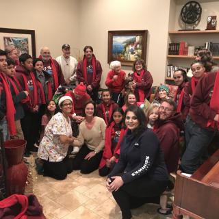 A group of people gathered indoors, wearing festive red scarves, likely celebrating a holiday.