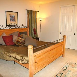 A cozy bedroom with a wooden bed frame, decorative pillows, a floor lamp, and artwork on the wall.