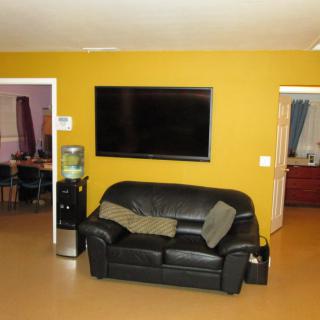 A cozy living room with a black sofa and a large television mounted on a yellow wall.